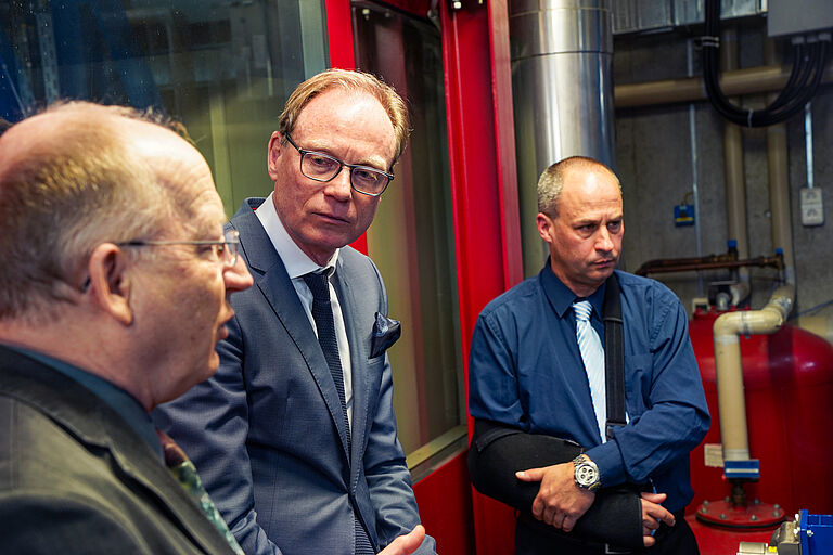 Drei Männer, in der Mitte der Staatssekretär stehen in einer Werkstatt im Gespräch.