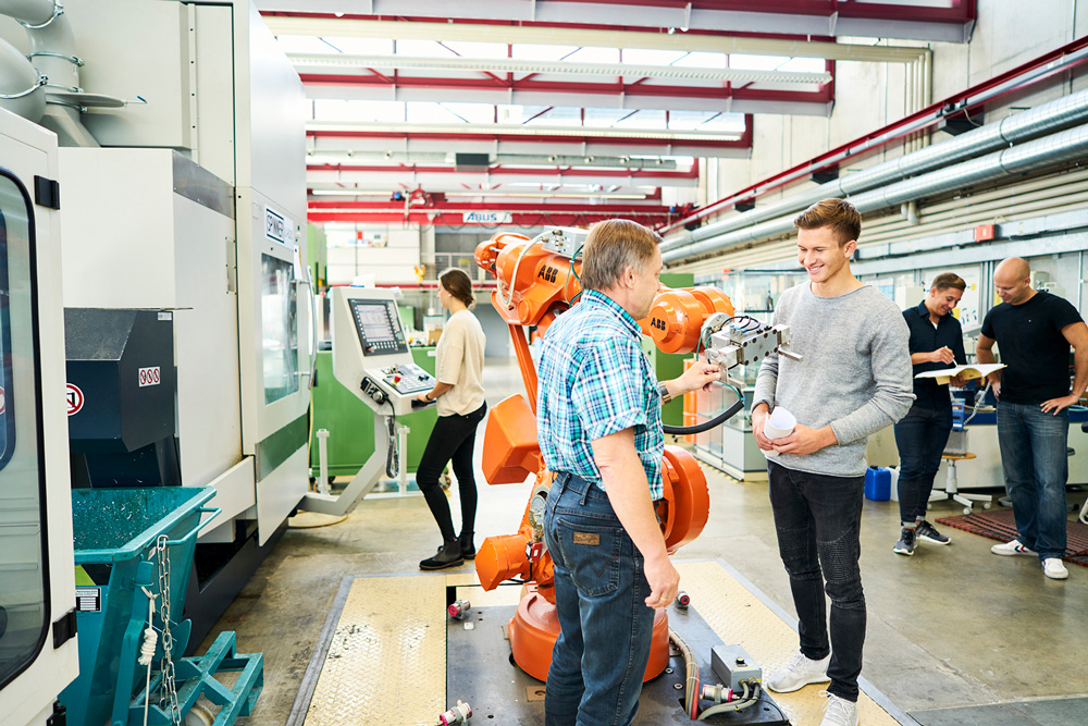 Personen in einer Maschienenhalle, die Industrieroboter bedienen