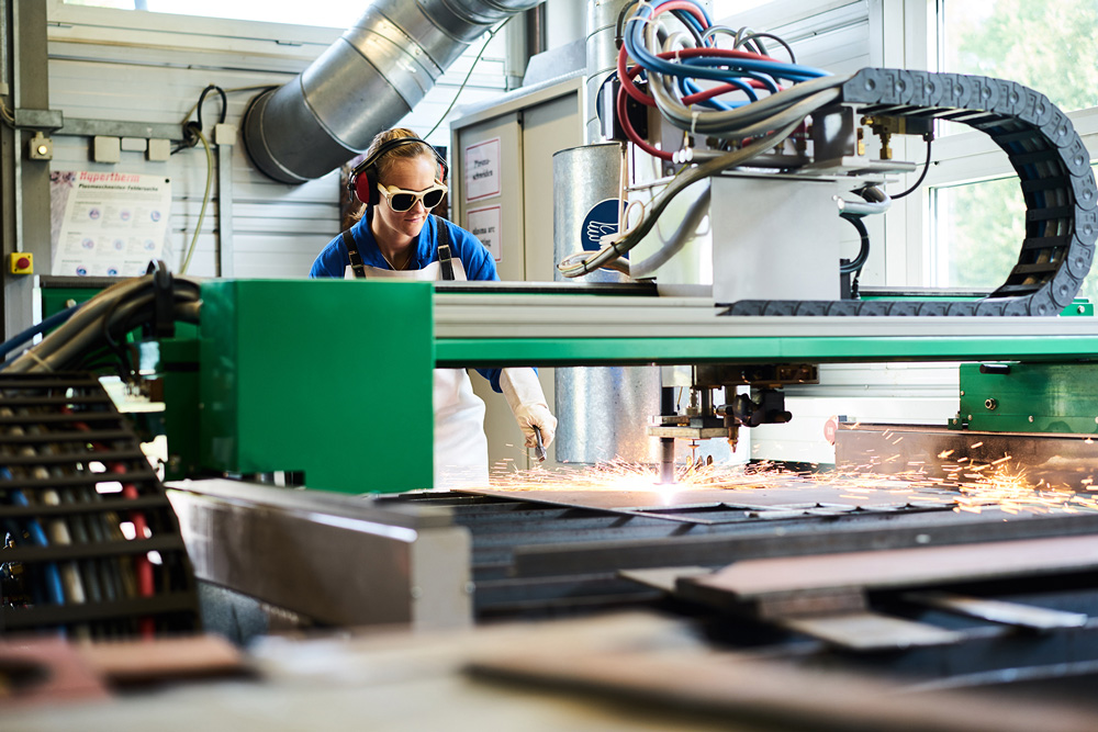 Studierende in Maschienenhalle, welche einen Plasmaschneider bedient