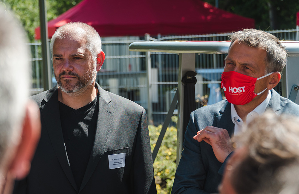 Personen in Anzügen in Gesprächsrunde vor Hochschulgebäude