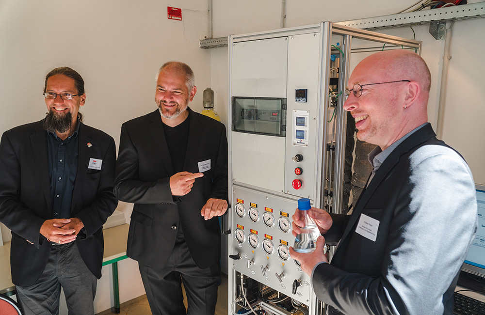 3 Personen in Anzügen vor einer Maschine zur Produktion von Methanol