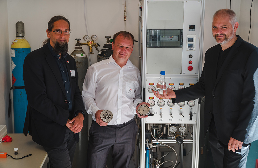 3 Personen in Anzügen vor einer Maschine zur Produktion von Methanol