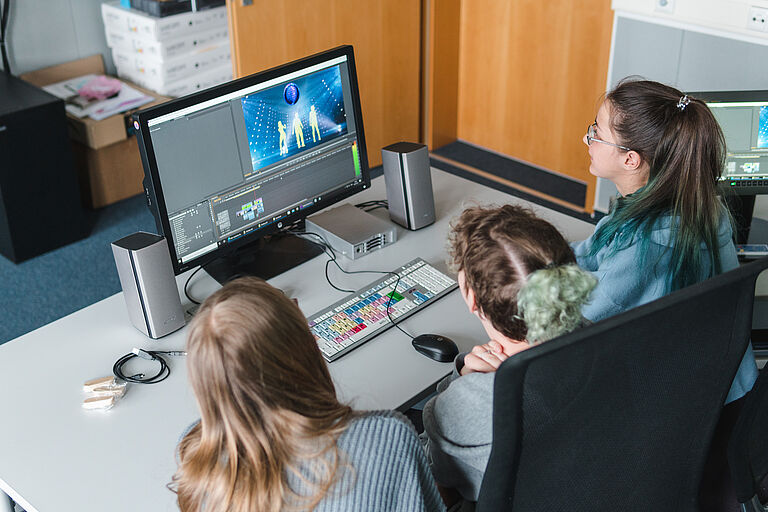Drei Mädchen sind schräg von hinten an einem Laptop zu sehen, man erahnt, dass es sich um eine Software handelt, mit der Video erstellt werden können.