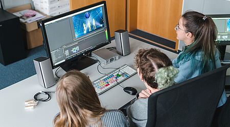 Drei Mädchen sind schräg von hinten an einem Laptop zu sehen, man erahnt, dass es sich um eine Software handelt, mit der Video erstellt werden können.