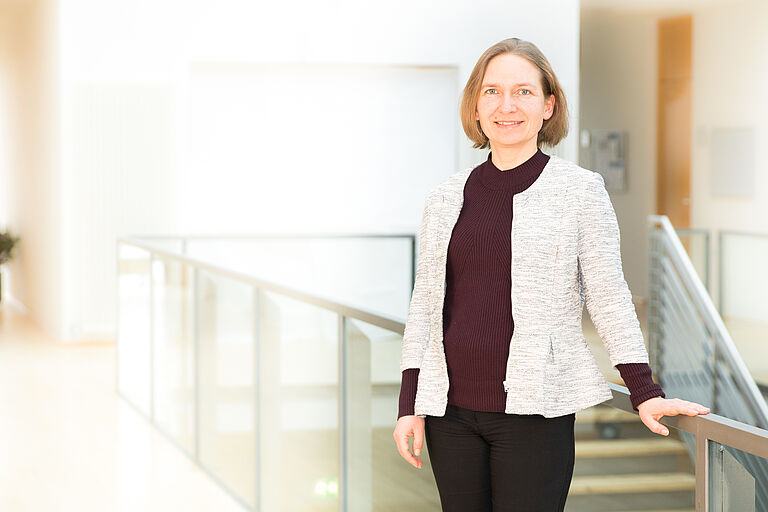 Das Portrait-Bild einer Frau in einem Fakultätsgebäude, eine Hand am Geländer einer Treppe