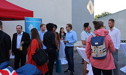 eine Gruppe von Menschen steht zusammen auf dem Campus der Hochschule - in Grüppchen im Gespräch und vor einem roten Pavillon