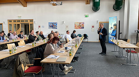 Menschen an Tischen, die einem Redner in einem Tagungsraum zuhören