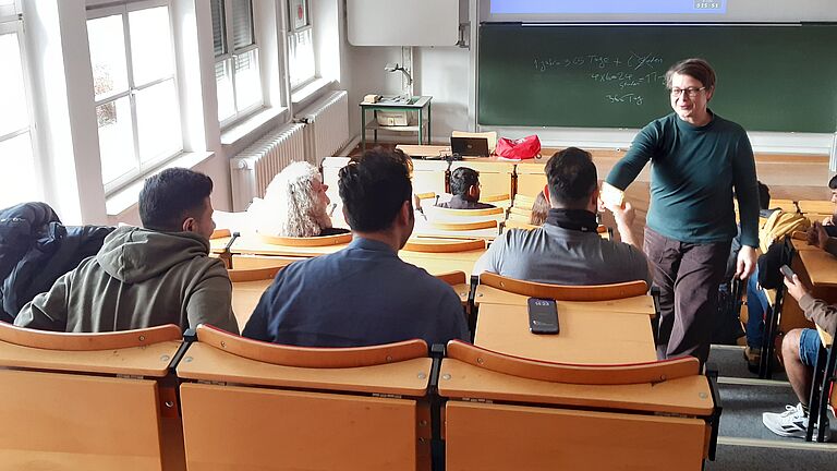 Eine Vertreter*in des Sprachenzentrums reicht einem Studierenden im Hörsaal lächelnd etwas an. 