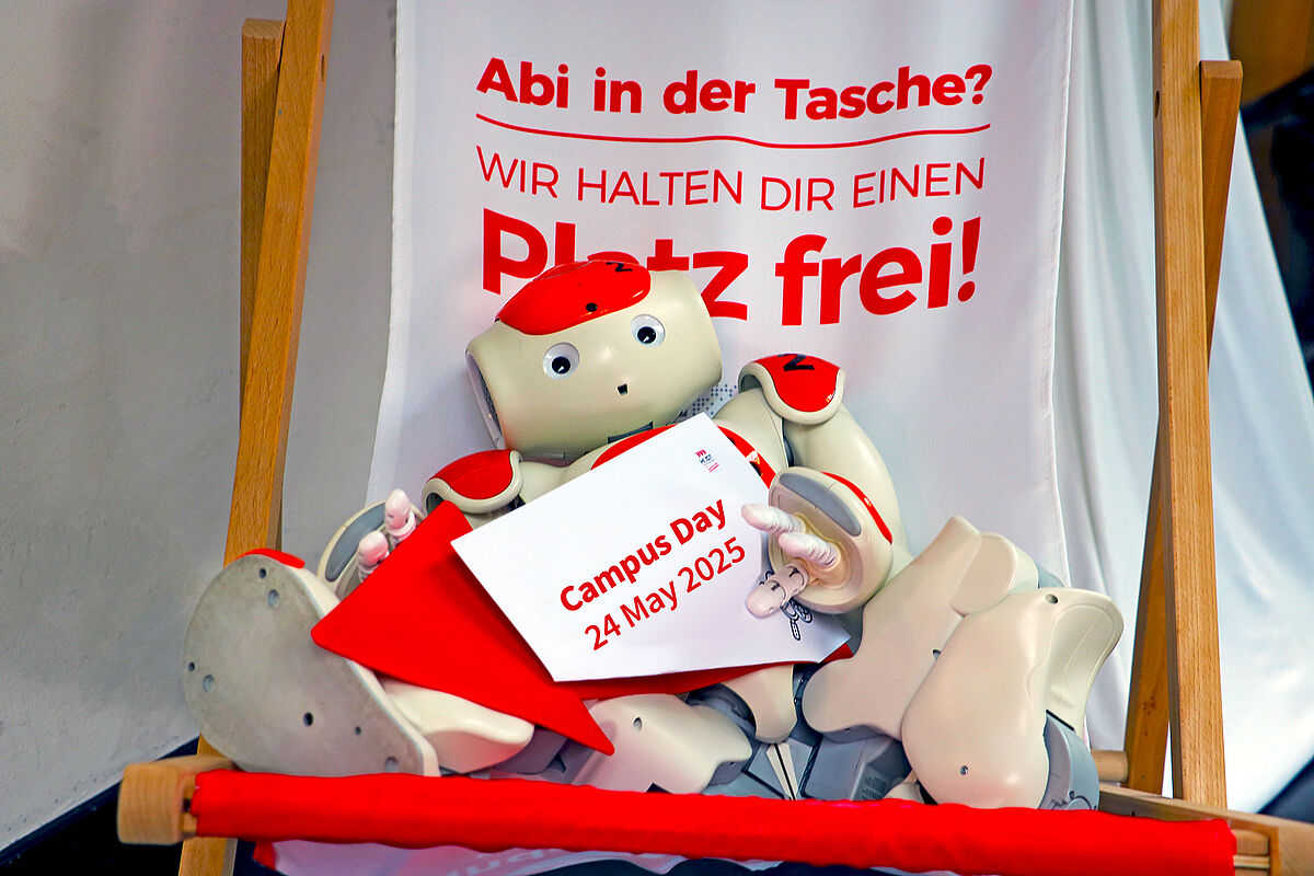 A robot sits in a deckchair holding a sign, Campus Day 24 May 2025