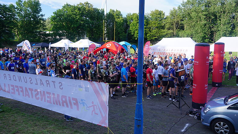 Viele Menschen an der Startlinie des Firmenstaffellaufs auf einem Sportplatz.