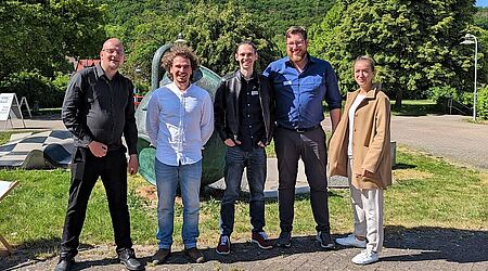 Fünf lächelnde Menschen - Das Team der HOST (v. l. n. r.): Martin Morgenstern, Torsten Wieck, Waldemar Adam, Jan Schmidt, Maria Freyer - stehen auf Asphalt im Grünen vor blauem Himmel