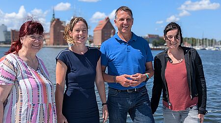 Vier Menschen (Eva-Maria Mertens, Dr. Sonja Gelinek, Prof. Dr. Ralph Sonntag und Heide Niemann) schauen freundlich in die Kamera, auf einem Schiffsdeck stehend, im Hintergrund der Sund.