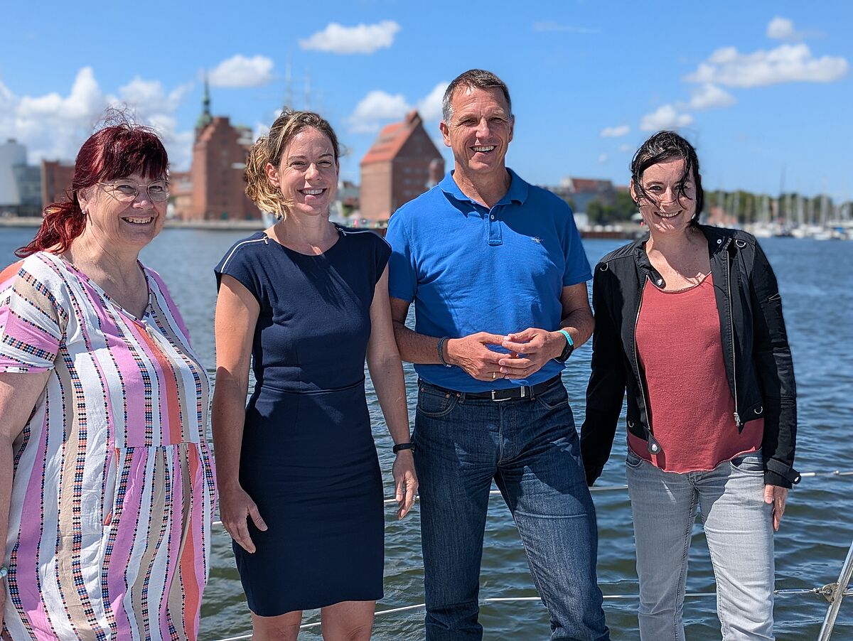 Vier Menschen (Eva-Maria Mertens, Dr. Sonja Gelinek, Prof. Dr. Ralph Sonntag und Heide Niemann) schauen freundlich in die Kamera, auf einem Schiffsdeck stehend, im Hintergrund der Sund.