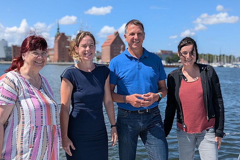 Vier Menschen (Eva-Maria Mertens, Dr. Sonja Gelinek, Prof. Dr. Ralph Sonntag und Heide Niemann) schauen freundlich in die Kamera, auf einem Schiffsdeck stehend, im Hintergrund der Sund.