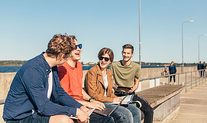 Studierende sitzen mit Laptop und Co. am Stralsunder Hafen, lernen, quatschen und haben Spaß dabei.