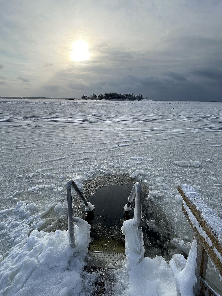 Eine Treppe mit Geländer führt in ein Loch im Eis in einem zugefrorenen Gewässer.