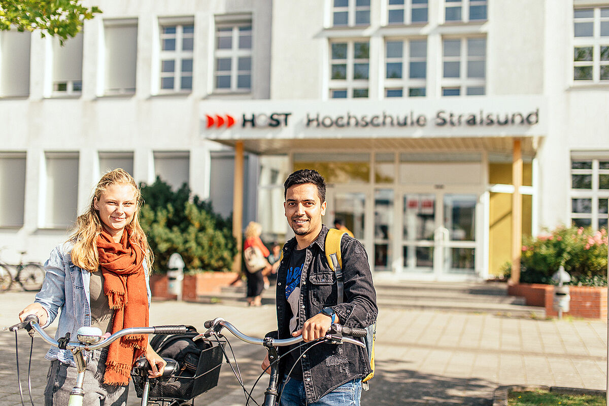 Students with bicycles on the campus of the Stralsund University of Applied Sciences in front of house 1