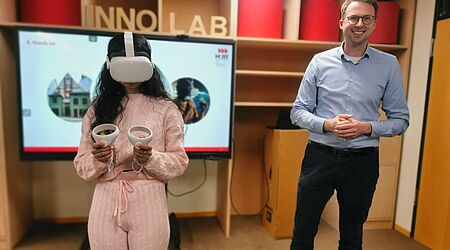 Eine junge Frau mit VR-Brille steht neben einem lächelnden Mann, Prof. Dr. Christian Piroutek