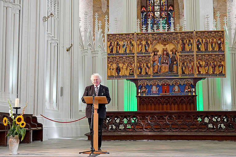 Ein Mann mit weißem Haar und Brille steht vor einem Redner-Pult in der Kirche