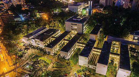 eine Aufnahme von oben zeigt mehrere Gebäude, die Universität Blumenau, bei Nacht, mit hellen Lichtern und dem Blick auf Palmen