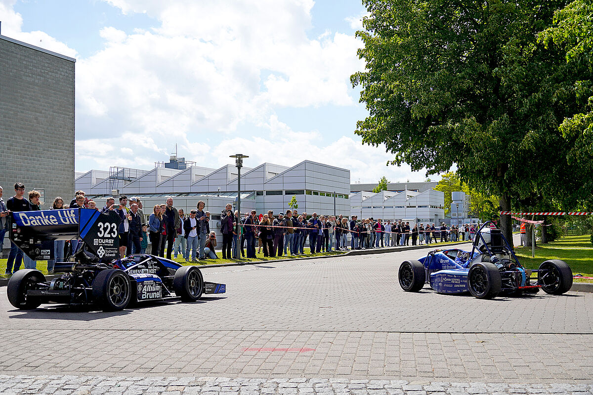 Zwei Fahrzeuge vom Baltic Racing Team positionieren sich um gleich zur Showfahrt zu starten. Besucher sind im Hintergrund hinter der Abspeerung.