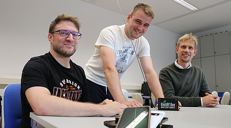 Drei Männer, die freundlich in die Kamera schauen, Handys vor sich auf dem Tisch: Prof. Dr. Andreas Noack, Justin Schnurbusch als wissenschaftliche Hilfskraft im Projekt und Prof. Dr. Jan Sölter