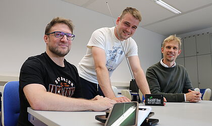 Drei Männer, die freundlich in die Kamera schauen, Handys vor sich auf dem Tisch: Prof. Dr. Andreas Noack, Justin Schnurbusch als wissenschaftliche Hilfskraft im Projekt und Prof. Dr. Jan Sölter