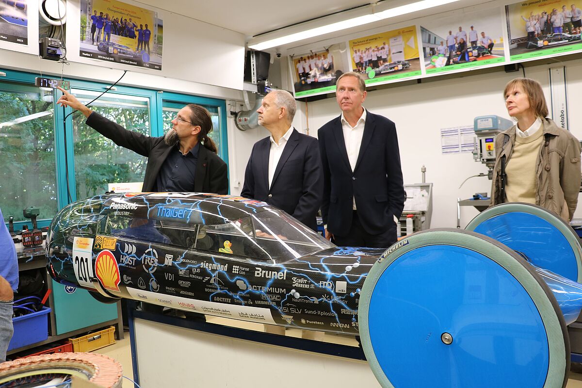 Besuch des litauischen Botschafters Giedrius Puodžiūnas beim ThaiGer-Racing-Team mit Heiko Miraß. Prof. Dr. Johannes Gulden erklärt den Antrieb und die Parameter des Wasserstoff-Rennwagens. 
