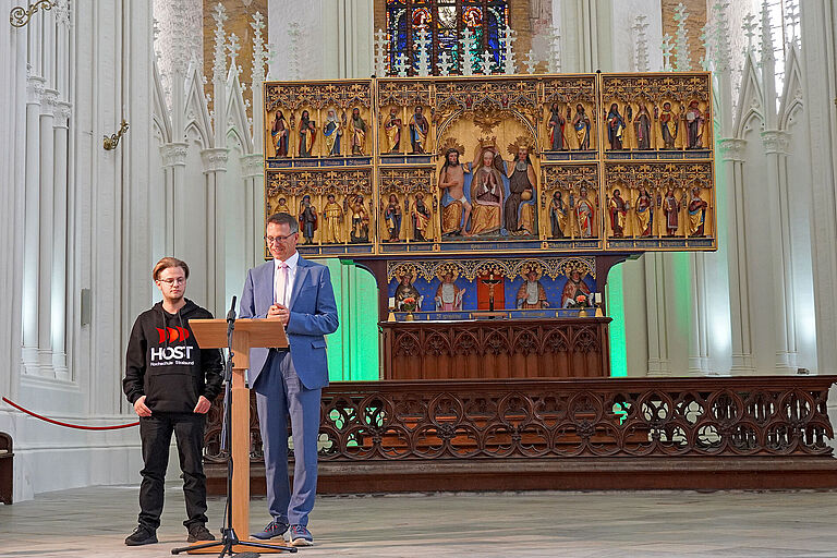 Ein junger Mann im Hoodie und ein Mann im Anzug stehen vor einem Rednerpult in einer Kirche.