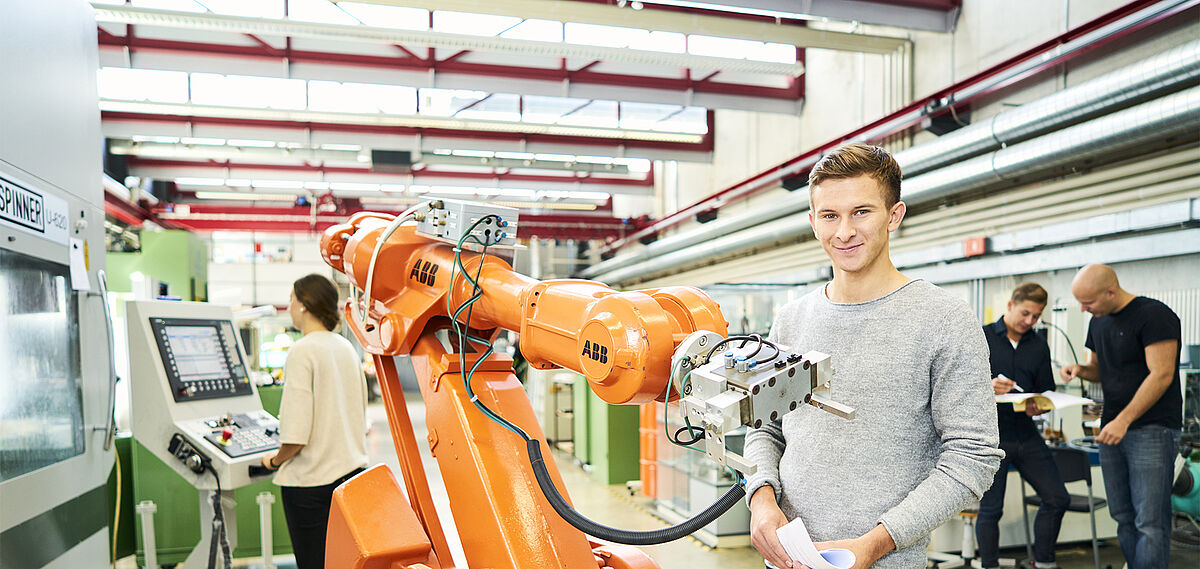 Student an einem modernen Industrie-Roboter sowie weitere Studierende in der Ausbildung im Labor Handhabungs- und Montagetechnik 