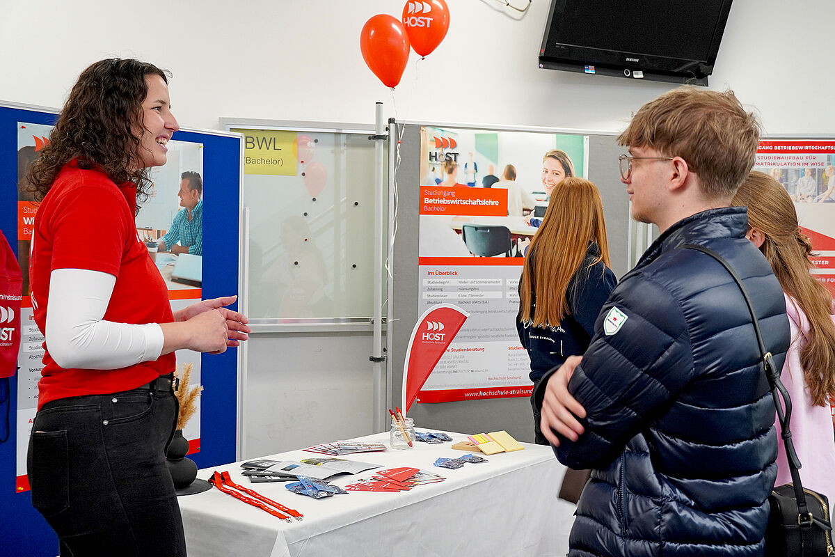 Studiengangs Koordinatorin berät zwei Besucher vor dem Infostand