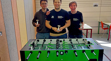 Drei Studenten halten den Pokal im Tischfussball in den Händen