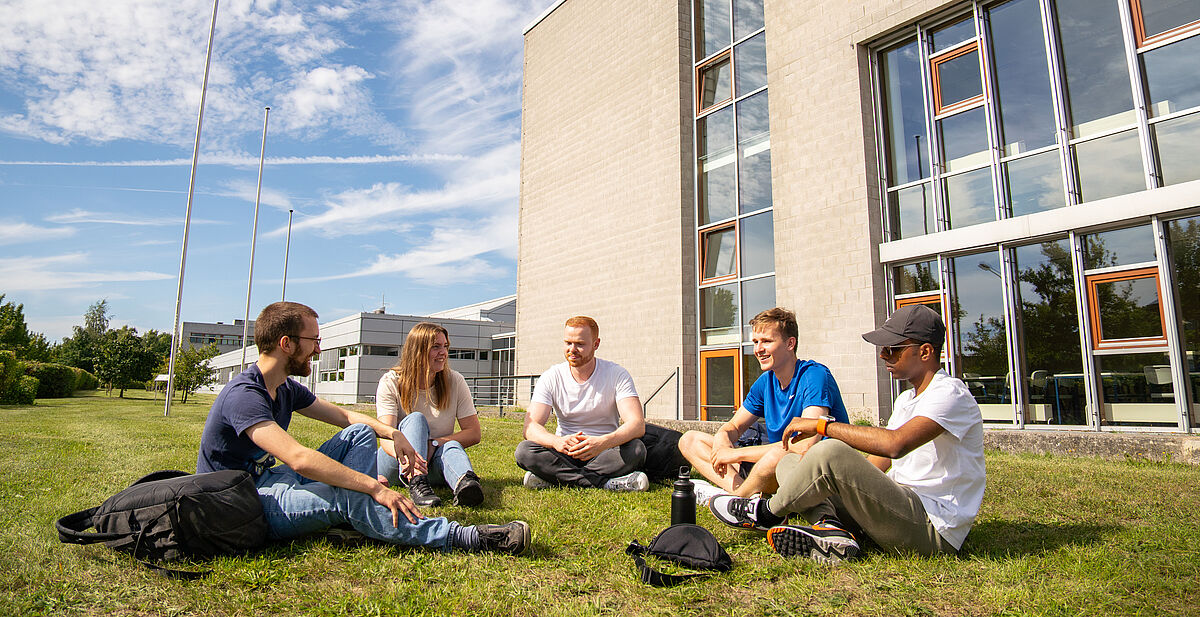 Studierende sitzen gemütlich im Rasen vor dem Gebäude der Fakultät Maschinenbau.
