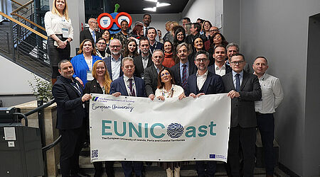 Ca. 3 Dutzend Menschen, in Anzügen und Blaisern, stehen auf einer Treppe, in einem Bürogebäude, und halten ein EUNICoast-Banner in die Kamera.