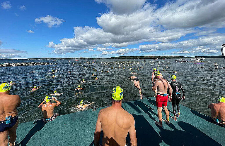 Blick auf den Strelasund mit unzähligen Schwimmern mit gelben Badekappen im Wasser und beim reinspringenzum Sundschwimmen 2021