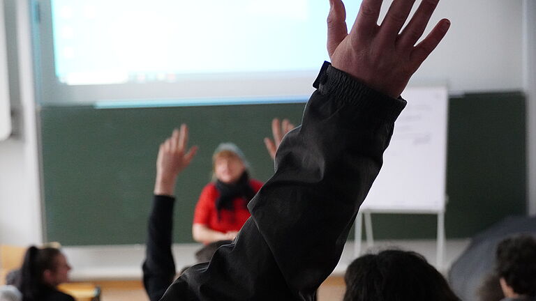 Studierende ragen die Hände in die Luft, im Hintergrund steht unscharf die Sportkoordinatorin