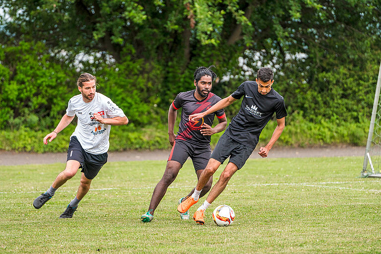 Drei Personen spielen Fußball auf einem grünen Rasen.