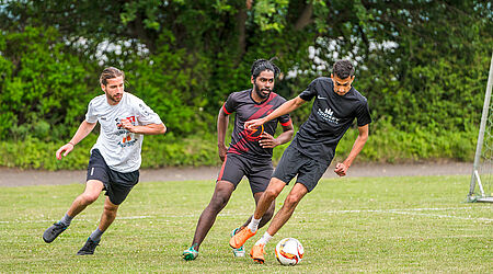 Drei Personen spielen Fußball auf einem grünen Rasen.