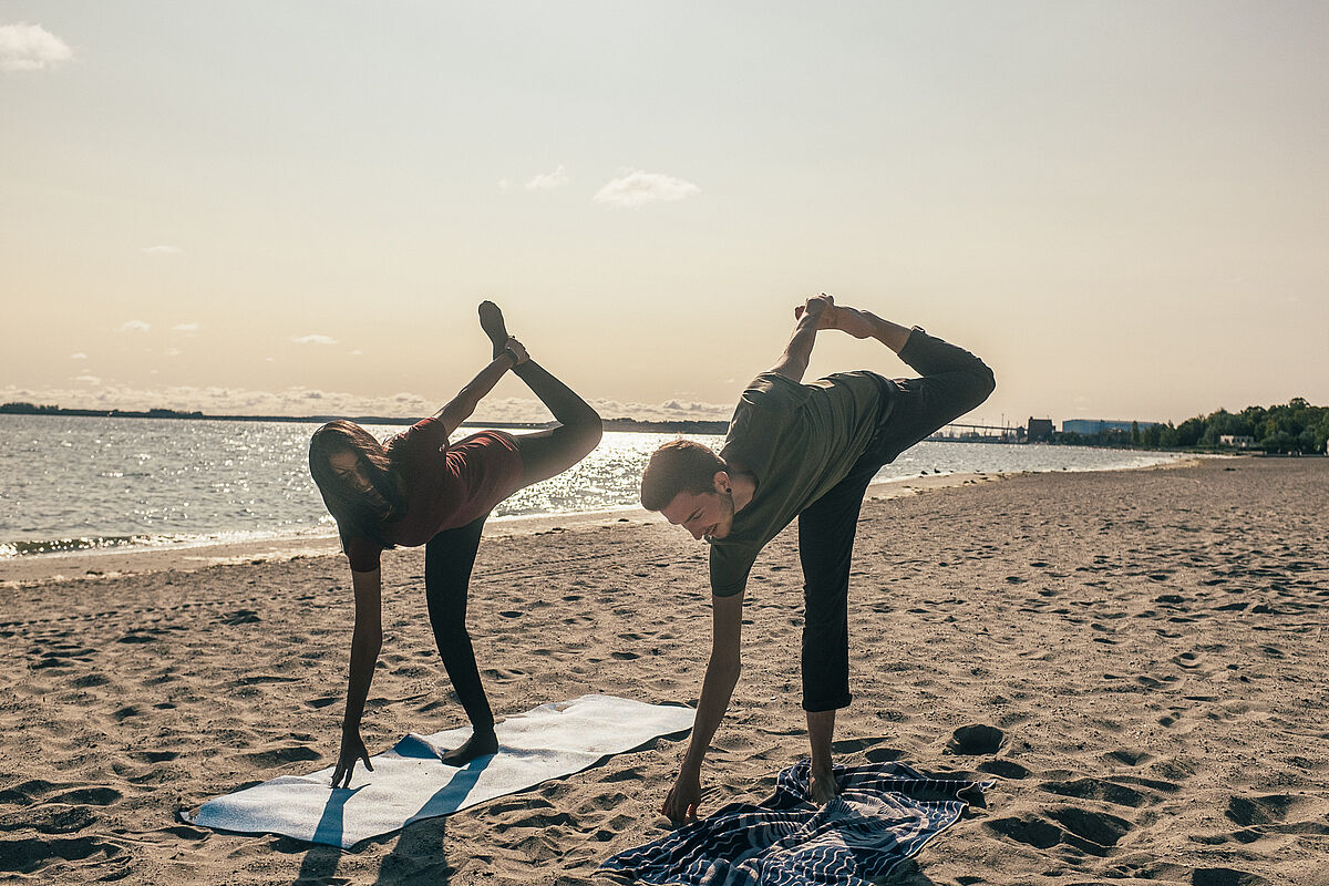Zwei Menschen machen Yoga am Strand