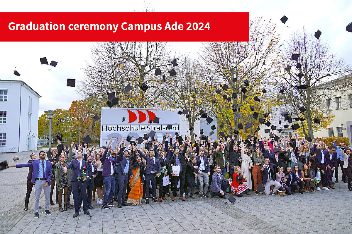Graduates in 2023 throwing their caps in the air together in front of a sign.