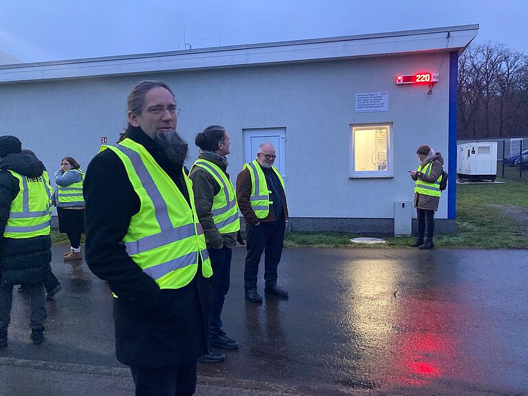 Mehrere Menschen mit Warnwesten bei regnerischem Wetter auf einer Außenanlage.