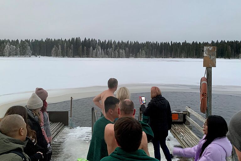Menschen am Rande eines zugefrorenen Gewässers vor einer Waldkulisse - der Auftakt zum Eisbaden.er