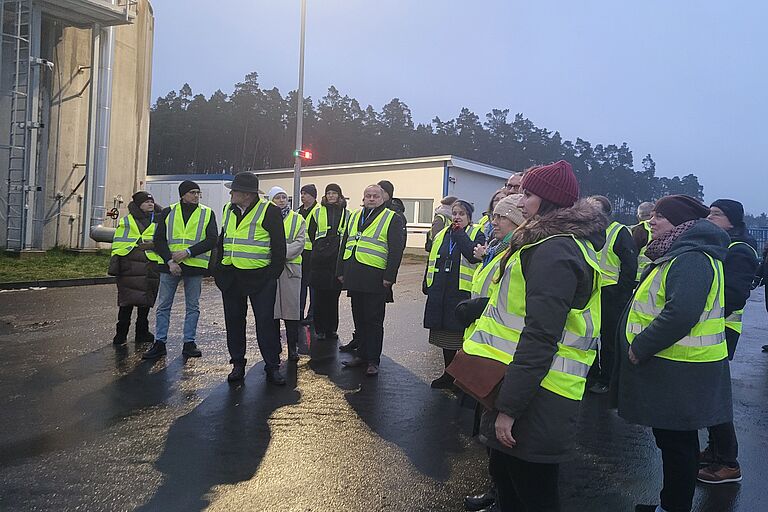 Mehrere Menschen mit Warnwesten bei regnerischem Wetter auf einer Außenanlage.