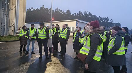 Mehrere Menschen mit Warnwesten bei regnerischem Wetter auf einer Außenanlage.