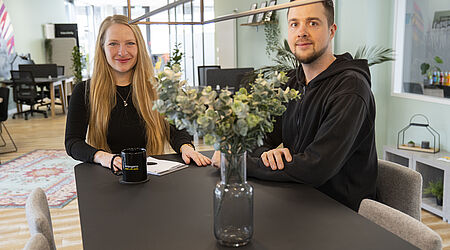 Eine Frau, Doreen Mdlodzik, und ein Mann, Lennart Deorocki, sitzen an einem Tisch.