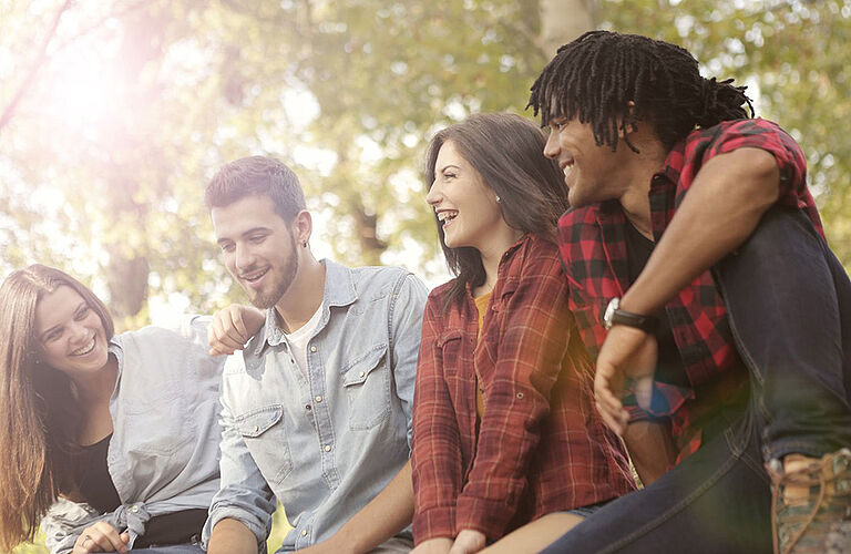 Vier lächelnde junge Menschen sitzen nebeneinander im Grünen - zwei Männer,  zwei Frauen, international