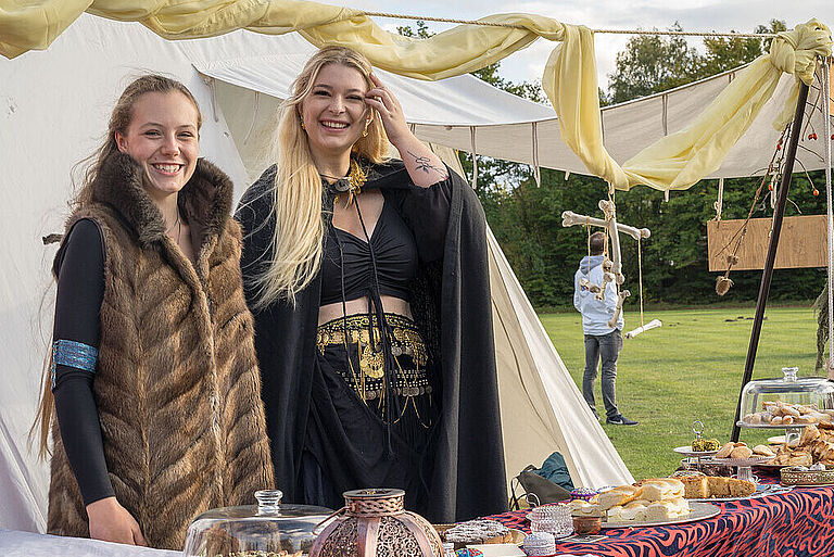 Zwei junge Frauen in Mittelaltergewand stehen an einem Buffet